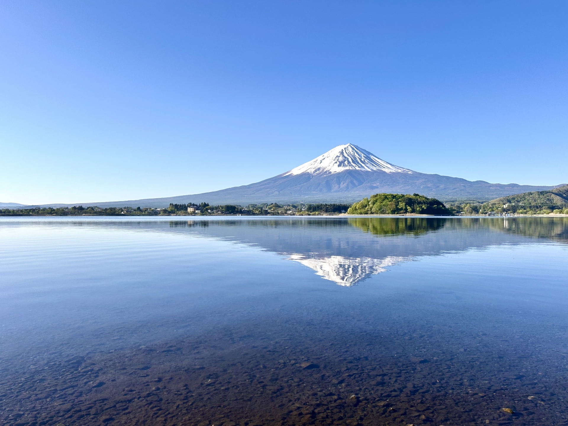 青空の下で河口湖の湖面に映る雪化粧の富士山と逆さ富士