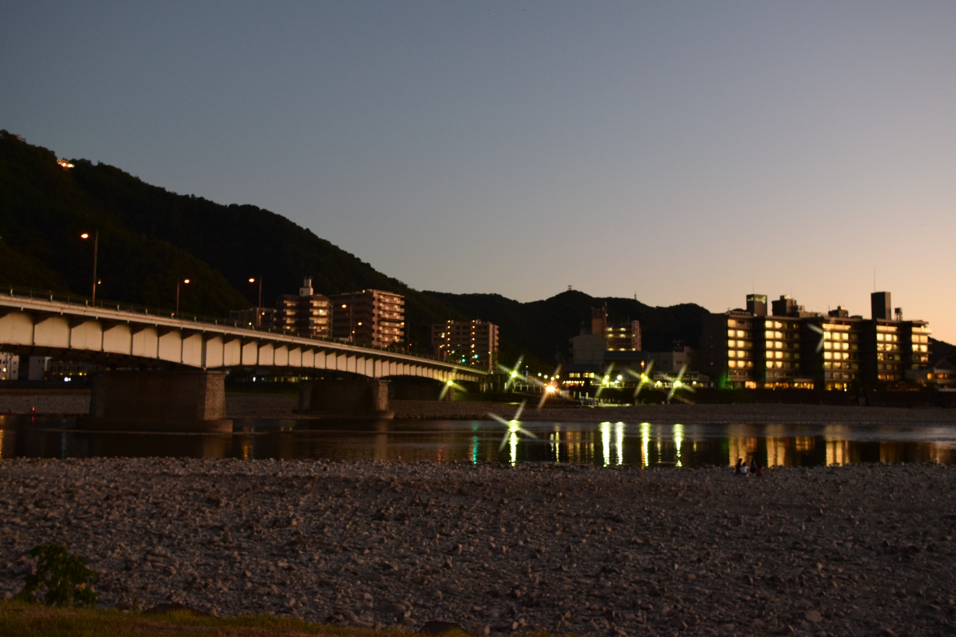 夕暮れの川に架かる橋と、川面に映る宿の明かり